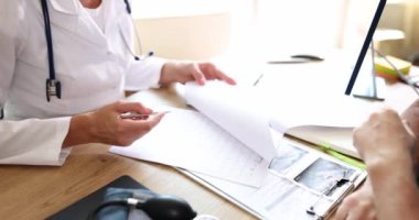 Steteskoplu aile doktoru erkek hasta tedavi planını açıklıyor ve soruları cevaplıyor. Kadın formu doldurur ve erkek ağır çekimde konuşur.