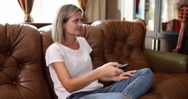 Oturma odasındaki kanepede oturan kadın uzaktan kumandayla TV 'de kanal değiştiriyor. Ev hanımı beklenmedik bir şekilde en sevdiği drama dizisine denk gelir ve sevinir.