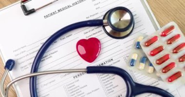 Kırmızı kalp oyuncak figürü steteskopun yanında yatıyor ve hasta tedavisi ile ilgili belgelerin üzerinde haplar var. Tıbbi ekipman ve kalp hastalıkları konsepti