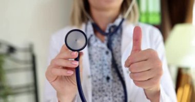 Memnun doktor steteskopu elinde tutuyor. Kadın, klinikte ağır çekimde duran tıbbi ekipmanların kullanılabilirliğini onaylıyor