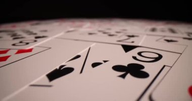 Poker destesi düzensiz bir şekilde hafif ışık altında yüzeye dağılmış. Yeni oyundan önce doğruluğu kontrol etmek için masaya konulan farklı takım elbiseli poker kartları