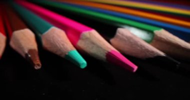 Keskinleştirilmiş çok renkli yeni çizim kalemleri karanlık yüzeyde yatıyor. Koyu arkaplanda çocuklar ve yetişkinler için çizim ve öğrenim amaçlı kırtasiye malzemesi