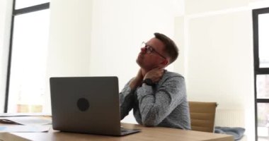 Çok çalışan adam, ofiste dizüstü bilgisayarla otururken baş ağrısı çekiyor. İşadamı, sıkı çalışmanın ardından kendini yorgun hissederek boyun eğiyor ve tapınakları ovalıyor.