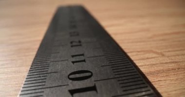 Tahta masadaki uzunluğu ölçmek için parmakları ve çizgileri olan metal cetvel. Odadaki masa başında tamirci var. Elle çalışan ustabaşı araçları