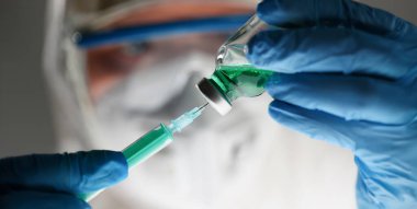 Koruyucu giysili ve eldivenli doktor şişeden şırıngaya ilaç alıyor. Covid 19 konseptine karşı aşının geliştirilmesi