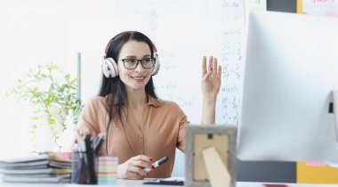 Kulaklıklı bir kadın bilgisayar ekranına el sallıyor. Çocuk kavramının uzaktan eğitimi