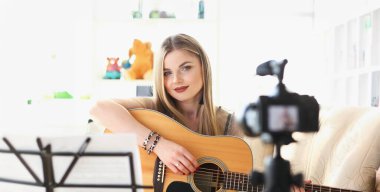 Kadın kamerada gitar çalıyor. Gitar çalmayı uzaktan öğrenme