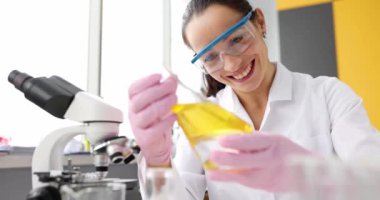 Gülümseyen bilim adamı laboratuardaki test tüpünde sarı yağı inceliyor. Kimya kliniğinde yağ ve kayganlaştırıcılar