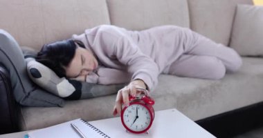 Kanepede uyuyan kadın çalar saati kapatır. Uykusuzluk, yorgunluk ve duyarsızlık.