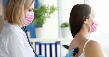 Tıbbi maskeli profesyonel bir doktor kadın hastanın akciğerlerini dinler. Akciğerlerin zatürree ve ilaç konseptinde incelenmesi.