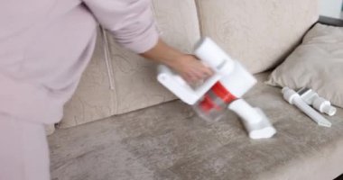 Oturma odasındaki kanepeyi temizlemek için beyaz kablosuz elektrik süpürgesi kullanıyor. Döşeme mobilya temizleme konsepti