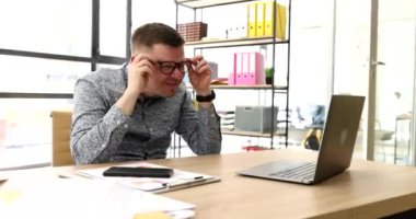 Gözlüklü bir iş adamı dizüstü bilgisayara bakıyor ve ofis 4K filminde şaşırtıcı. Çevrimiçi olumsuz haber kavramı