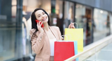 Bayan alışverişin portresi akıllı telefondan paketle dışarıda oturan bir arkadaşla konuşuyor. Bir sürü renkli paketler var. Satış, alışveriş, indirim konsepti