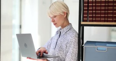 Konsantre sarışın kadın kişisel bilgilerini dizüstü bilgisayarından, rafın yanındaki bilgisayardan giriyor. Genç yönetici yavaş çekim programı kullanmak için çevrimiçi kayıt yapıyor