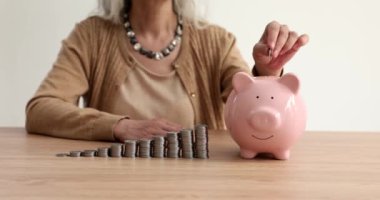 Olgun kadın masadaki pembe kumbaraya bozuk para atıyor. Para konteynırının yanına konmuş bozuk paralar. Finansal tasarruf ve birikim