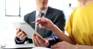Adamın elinde ortak istatistiklerini gösteren tablet var. Kadın, masa ağır çekimde oturan elektronik cihazın kalemini ekrana doğrultuyor