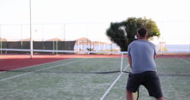 Sportif adam küçük sarı topa tenis raketiyle vuruyor. Erkek kişi tenis kortunda rakibiyle spor oyunu oynamaktan hoşlanır.