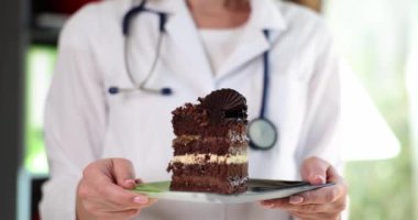 Kadın doktor elinde lezzetli çikolatalı pastayla tabağı tutuyor. Beyaz laboratuvar önlüklü kadın tatlı gösteriyor. Sağlıksız yeme konsepti