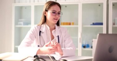 Masada oturan gözlüklü doktorun hastayla görüntülü konuşması. Genç kadın çevrimiçi sağlık tavsiyeleri veriyor