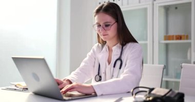 Masada oturan dizüstü bilgisayarlı kadın terapist tipleri. Genç kadın hastaların bilgilerini yavaş çekimde kontrol ediyor.