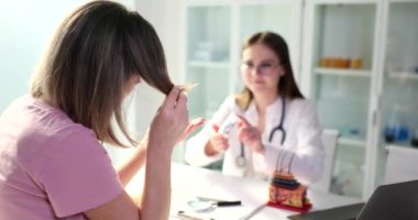 Deneyimli trikoloğum saç dökülmesinden muzdarip kadın hastaya vitamin veriyor. Kadın uzman, ilgili kadına ağır çekimde ilaç yazıyor.