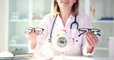 Oftalmolog görüş düzeltmesi için gözlük seçimi öneriyor. Dost canlısı kadın uzman elinde gözlüklerle ağır çekimde gülümsüyor.