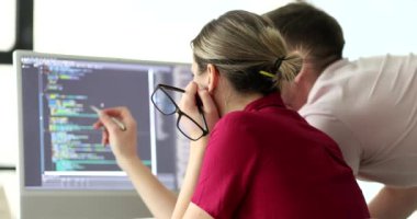 Bayan programcı, meslektaşına bilgisayar ekranında web sitesinin kodunu gösteriyor. Kadın ve erkek yavaş çekimde cihazın ekranına bakın