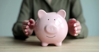 Kadın ellerini pembe kumbaranın kenarlarına koyuyor ve tahta masada bozuk paralarla sarılıyor. Tasarruf ve yavaş çekim birikimi için para konteynırına sevgi
