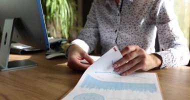 Sekreter, ahşap masada oturan panodaki istatistiklerle soruşturma kağıtlarını çeviriyor. Kadın yazılı belgelerin bilgilerini yavaş çekimde kontrol ediyor