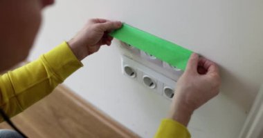 Foreman, duvarları boyarken prizleri yeşil bant ile kapatıyor. Profesyonel uzman, ağır çekimde oturma odasında tadilat yapıyor.