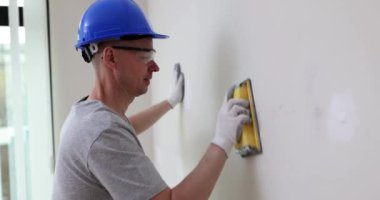 Mavi kasklı ustabaşı oturma odasındaki beyaz duvarları aletle işliyor. Gözlüklü ve koruyucu eldivenli odaklı işçi yavaş çekimde tadilat yapıyor.