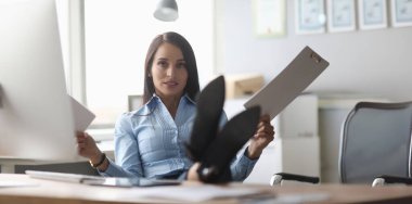 Şirin bayanın şirket ofisindeki portresi. Çok çalışan iş kadını elinde iş belgesi tutuyor ve sakin bir şekilde kameraya bakıyor. İş kadını sandalyede oturuyor ve ayaklarını masaya koyuyor.