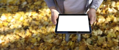 Pakr 'daki adam dijital tablet bilgisayarını sarı yapraklı arka plan görüntüsüne karşı parktaki boş ekranla tutuyor. Sonbahar satış kavramı