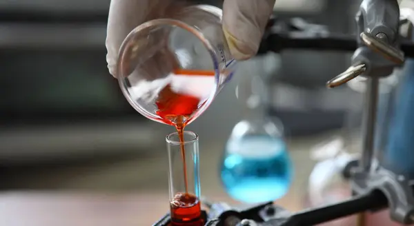 stock image Focus on male hand in sterile gloves holding bulb. Pharmaceutist transfusing red fluid in glass flask. Medicine experiments and researches concept. Blurred background