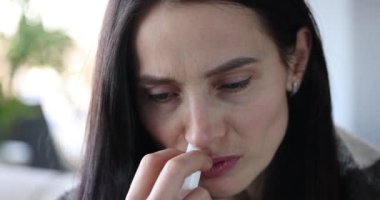 Woman with runny nose holds medicine in hand and puffs into red nose. Treatment of severe runny nose or allergies concept