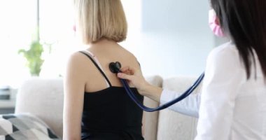 Doctor listens to patient lungs from back at home. Cold cough and pneumonia concept