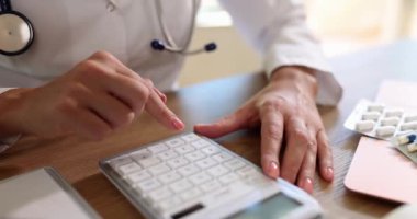 Doktor tüm masrafları hesaplamak için hesap makinesi kullanıyor. Sağlık sigortası maliyeti