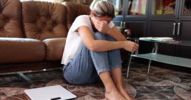 Depresyon ve nevrozdan muzdarip bir kadın yerde oturup ağlıyor. Aşırı stres ve hormon yetmezliği.