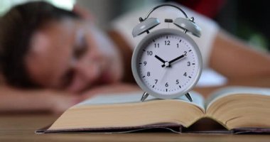 Kitaptaki çalar saat ve uyuyan kadın. Eğitim zamanı ve öğrenme ve uyku