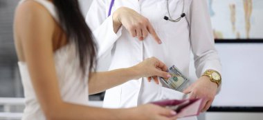 Close-up of female hand putting money to doctor pocket. Patient paying medical service. Bribe to practitioner. Corruption in medicine