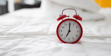 Close-up of red alarm clock at 7 oclock on bed. Early morning, daily regime and working day. Lack of sleep idea. Alarm-clock morning wake-up time concept clipart