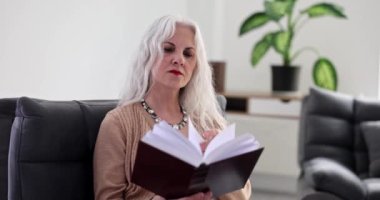 Sakin Crey saçlı kadın kitap okuyor. Ağır çekimde koltukta oturuyor. Olgun bayan ilginç romanların tadını çıkarırken rahatlıyor. Hobi ve eğlence yaşam tarzı
