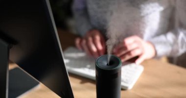 Ahşap masadaki klavyede dağıtıcı koku yayarken kadın bilgisayarda yazı yazıyor. Freelancer evde çalışıyor ve ağır ağır aromanın tadını çıkarıyor.