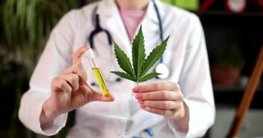 Kadın doktor elinde taze kenevir yaprağı ve elinde yağ bulunan bir tüp tutuyor. Üniformalı kadın, alternatif ilaç olarak ağır çekimde psikoaktif ilaçlar gösteriyor.