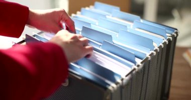 Kadın, şirket arşivindeki kart indeks kutusunda dosya arıyor. Ofis çalışanı sözleşmeyi bulmak için belgeleri kontrol ediyor. Şirkette organize evrak sistemi