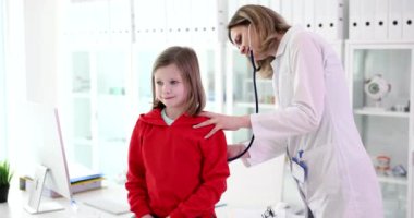 Doktor küçük kızı steteskopla ağır çekimde muayene ediyor. Çocuk doktoru, çocuğun kalp atışlarını ve nefes alışlarını kontrol ediyor. Sağlık hizmetleri