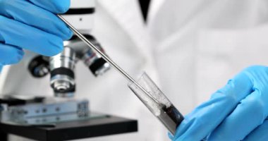 Laboratuvar çalışanı demir çubuklu gübre hapını mikroskop yakınındaki siyah toprakla birlikte boruya koyar. Lastik eldivenli kadın, bilimsel araştırmalar için yavaş çekim örnekleri hazırlıyor.