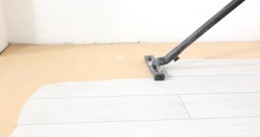 İşçi odada endüstriyel temizlik yapmak için elektrikli süpürge kullanıyor. Adam, ağır çekimde öğüttükten sonra talaş temizlemek için beyaz lamine zemini vakumlar.