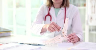 Kadın, masada oturan iskelet bileğin yapay modelindeki kemiklere işaret ediyor. Steteskoplu bir doktor insan vücudunun yavaş çekim yapısını inceliyor.