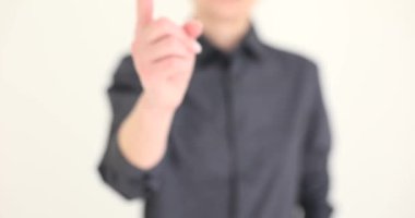 Klasik gri gömlekli kadın işaret parmağıyla bej arka planda duran kameraya işaret ediyor. Bulanık kadın hareketi yavaş çekimde yapar.